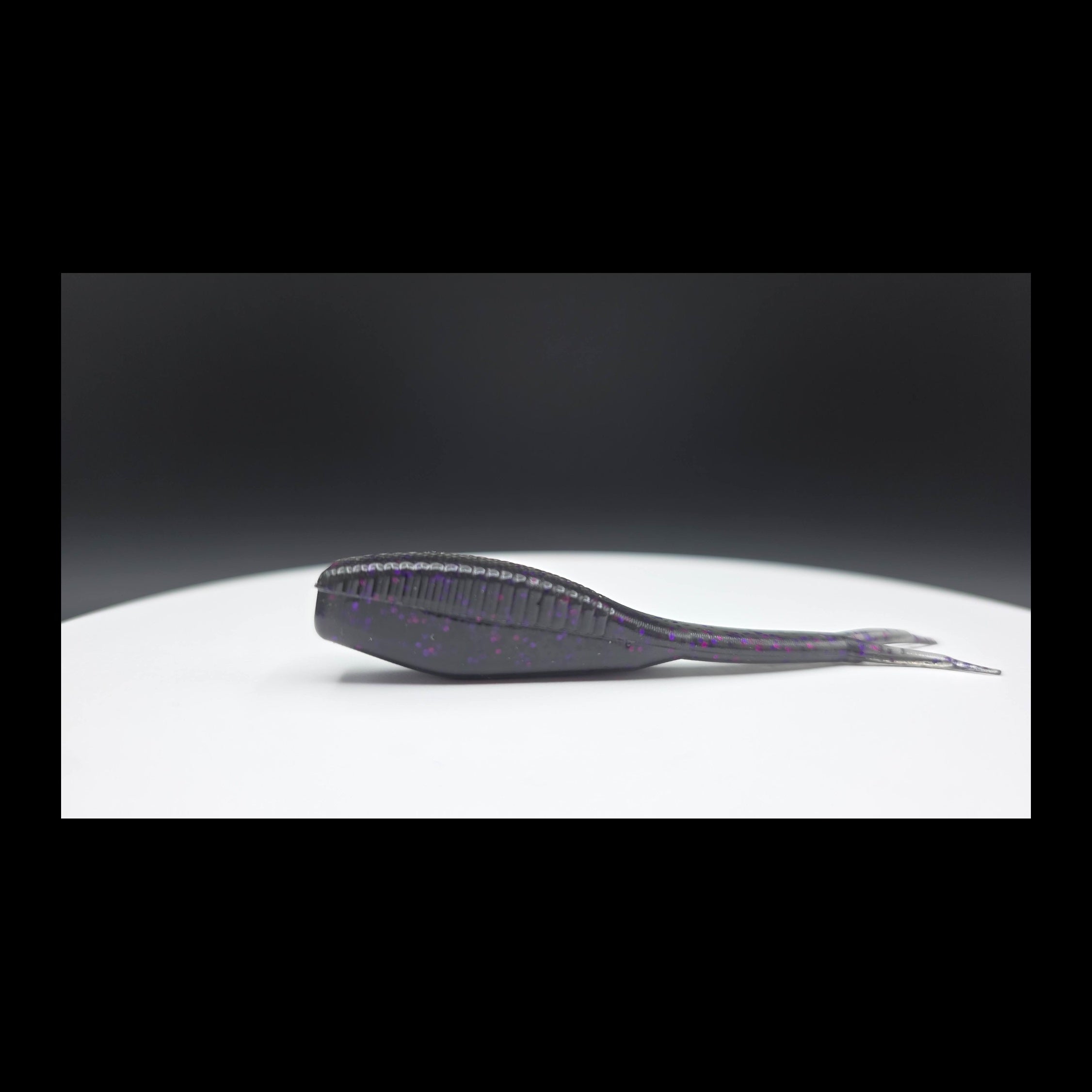 Black fishing lure with purple and red glitter on a white surface with a dark background