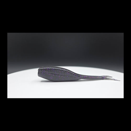 Black fishing lure with purple and red glitter on a white surface with a dark background