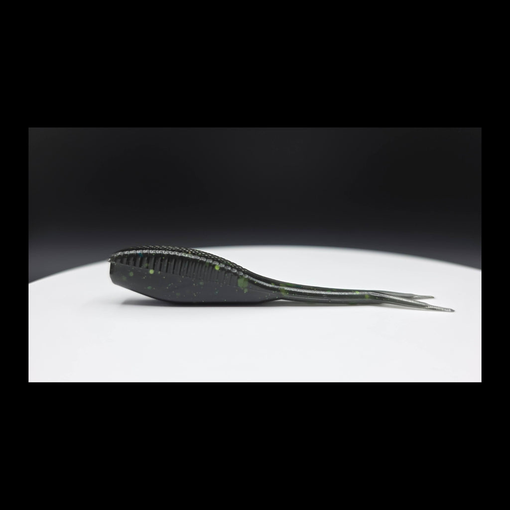 Black fishing lure with green glitter on a white surface with a dark background