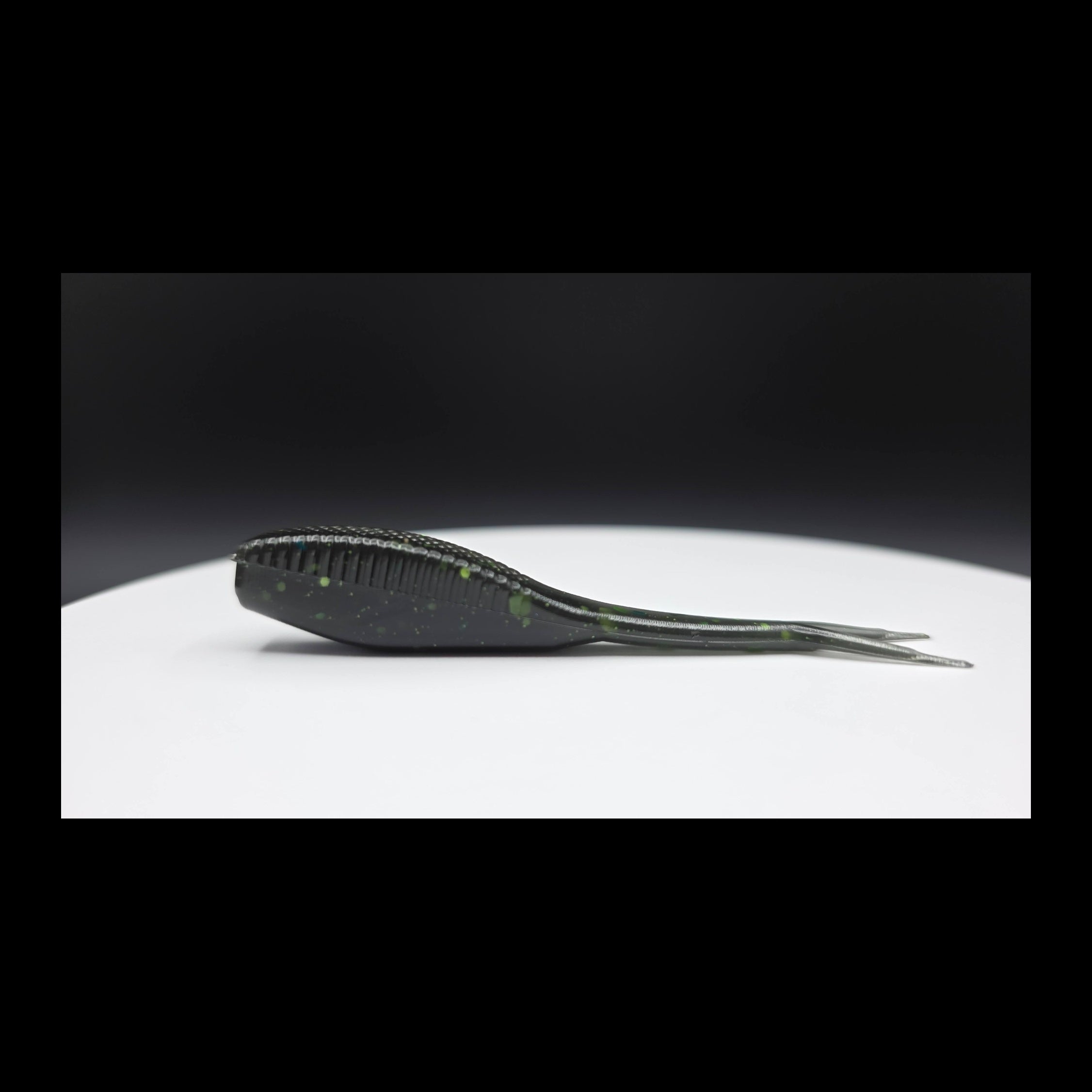 Black fishing lure with green glitter on a white surface with a dark background