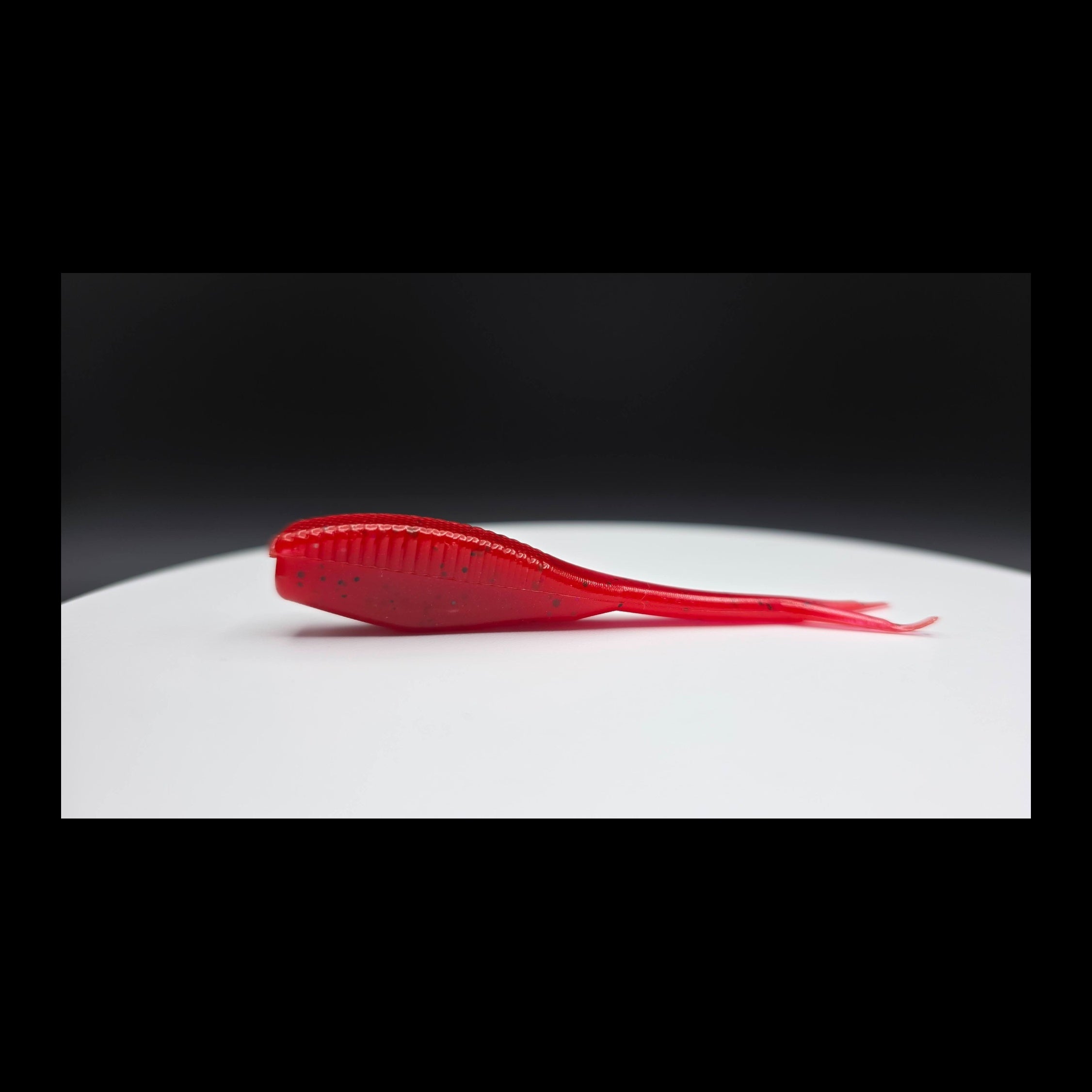 Red fishing lure with black glitter on a white surface with a dark background