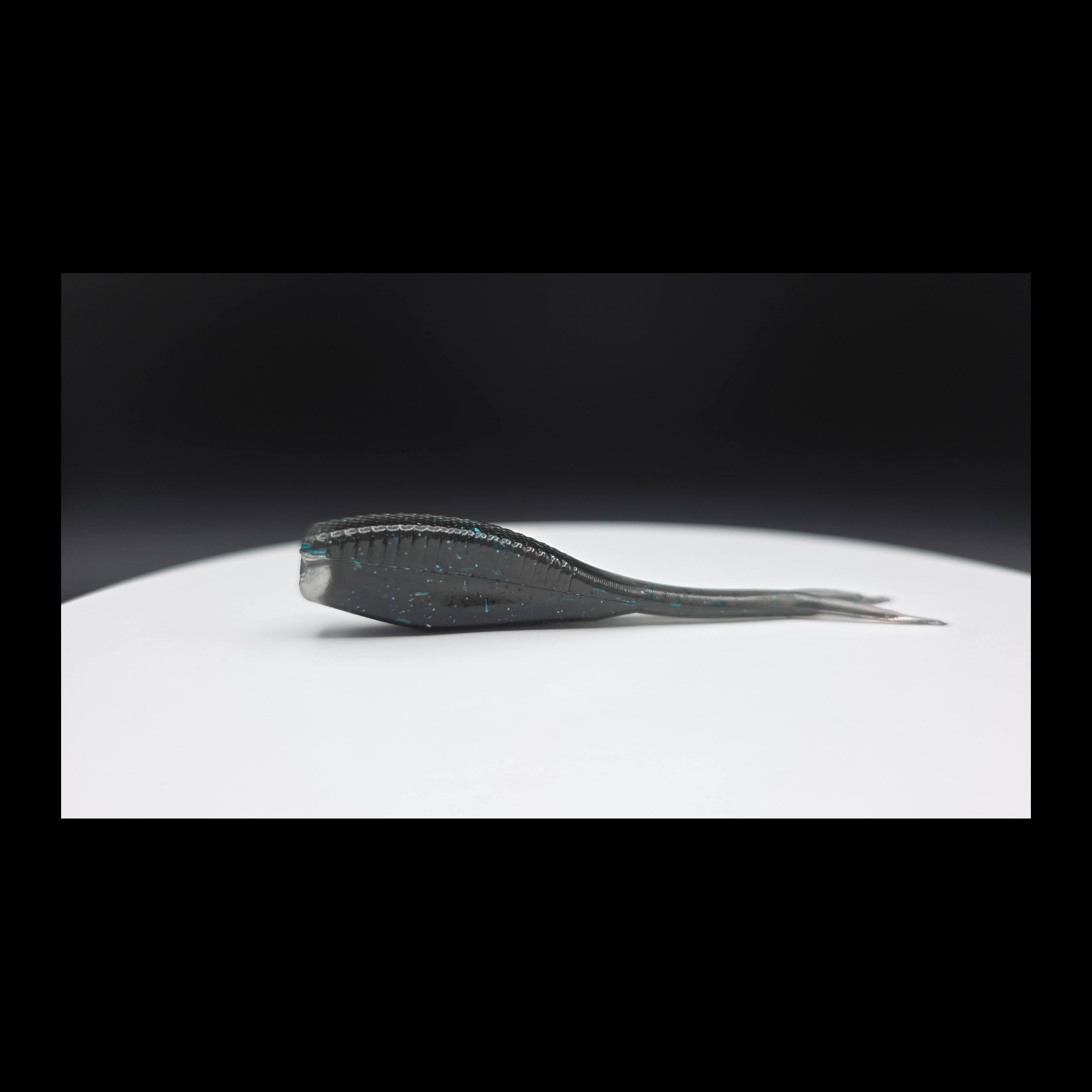 Black fishing lure with blue glitter on a white plate with a dark background