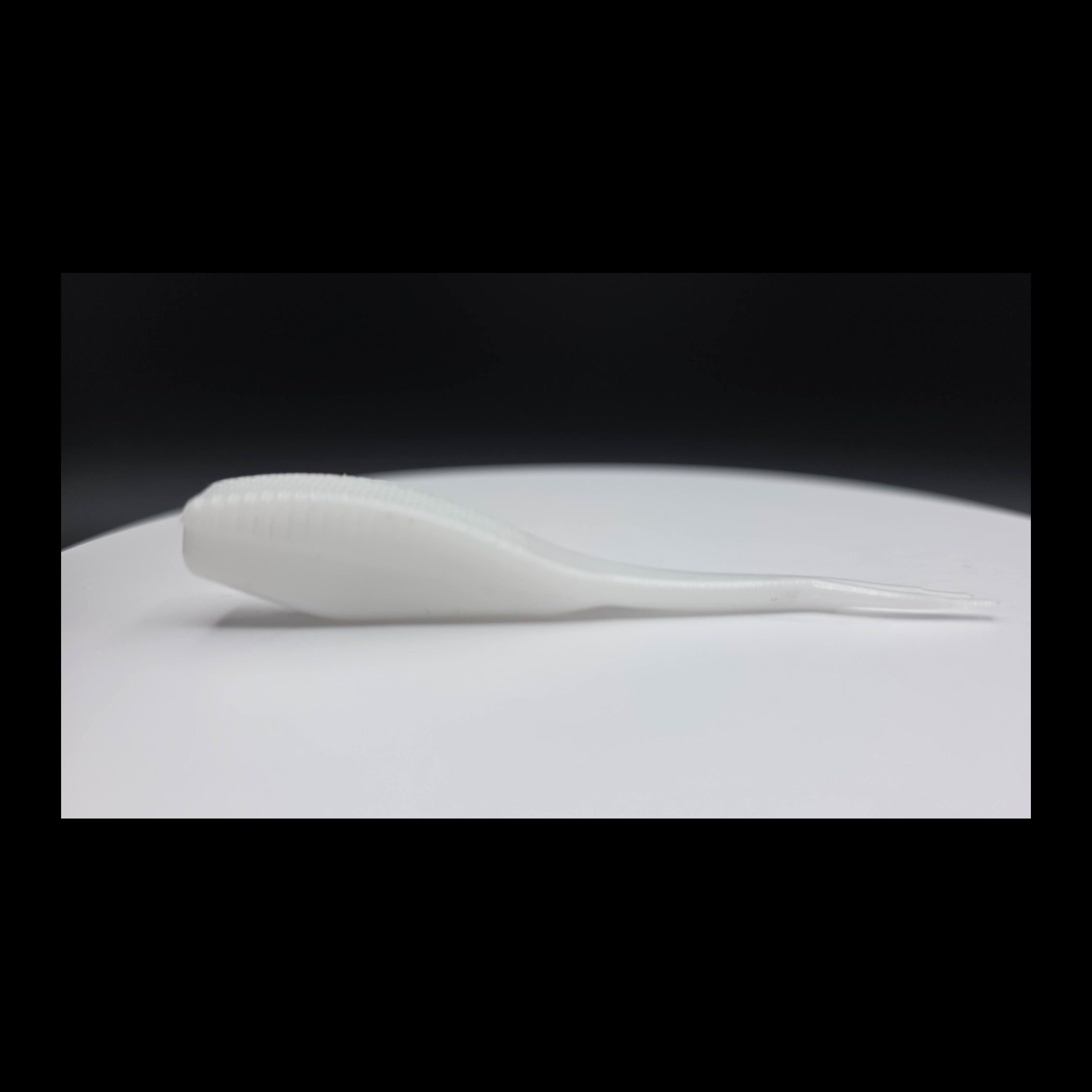 White fishing lure on a white surface with a black background