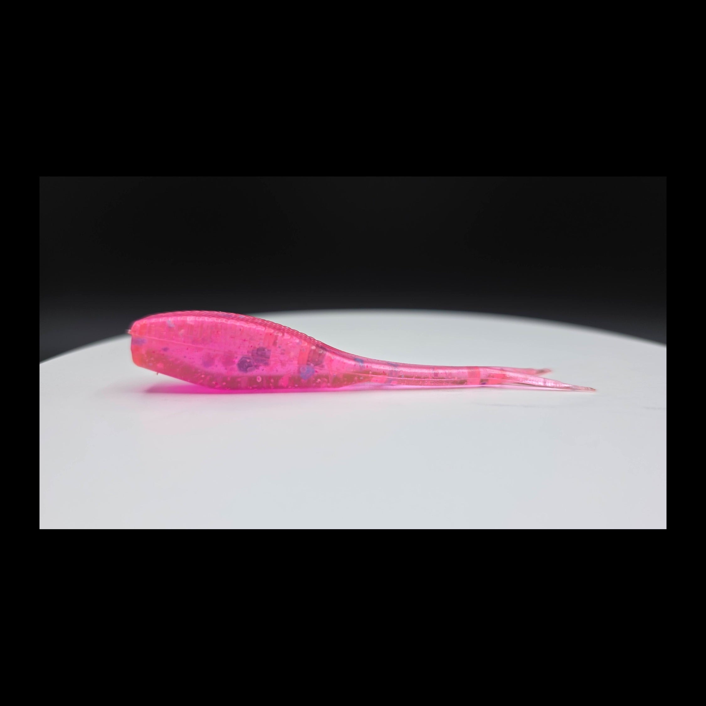 Pink fishing lure with colored glitter  on a white plate with a black background