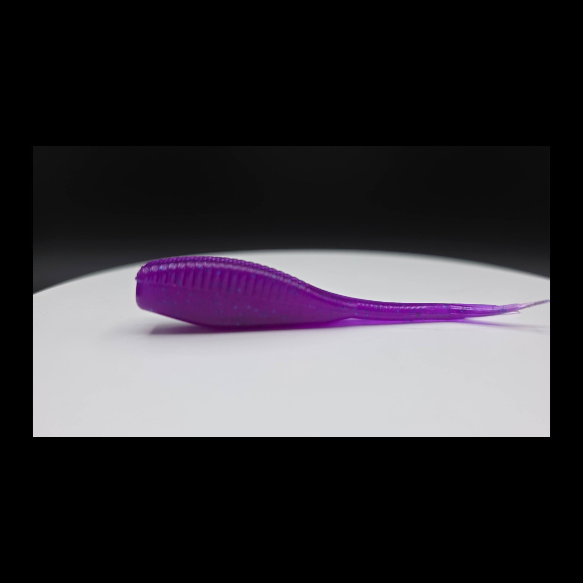 Purple lure with blue glitter on a white surface with a black background