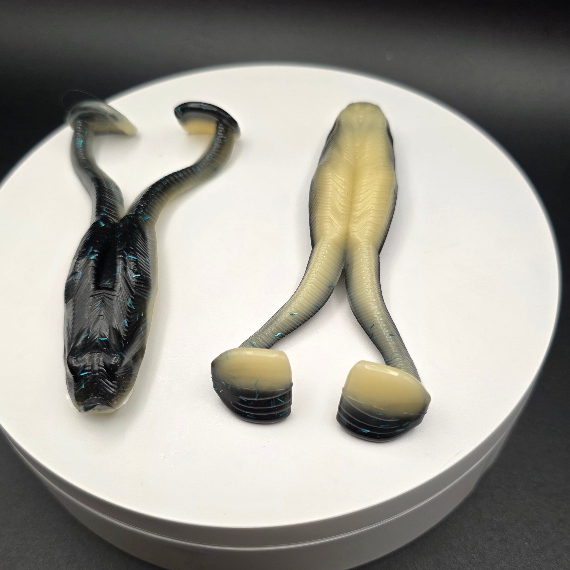 Black and Bone colored fishing lures with blue glitter on a white circular base against a dark background