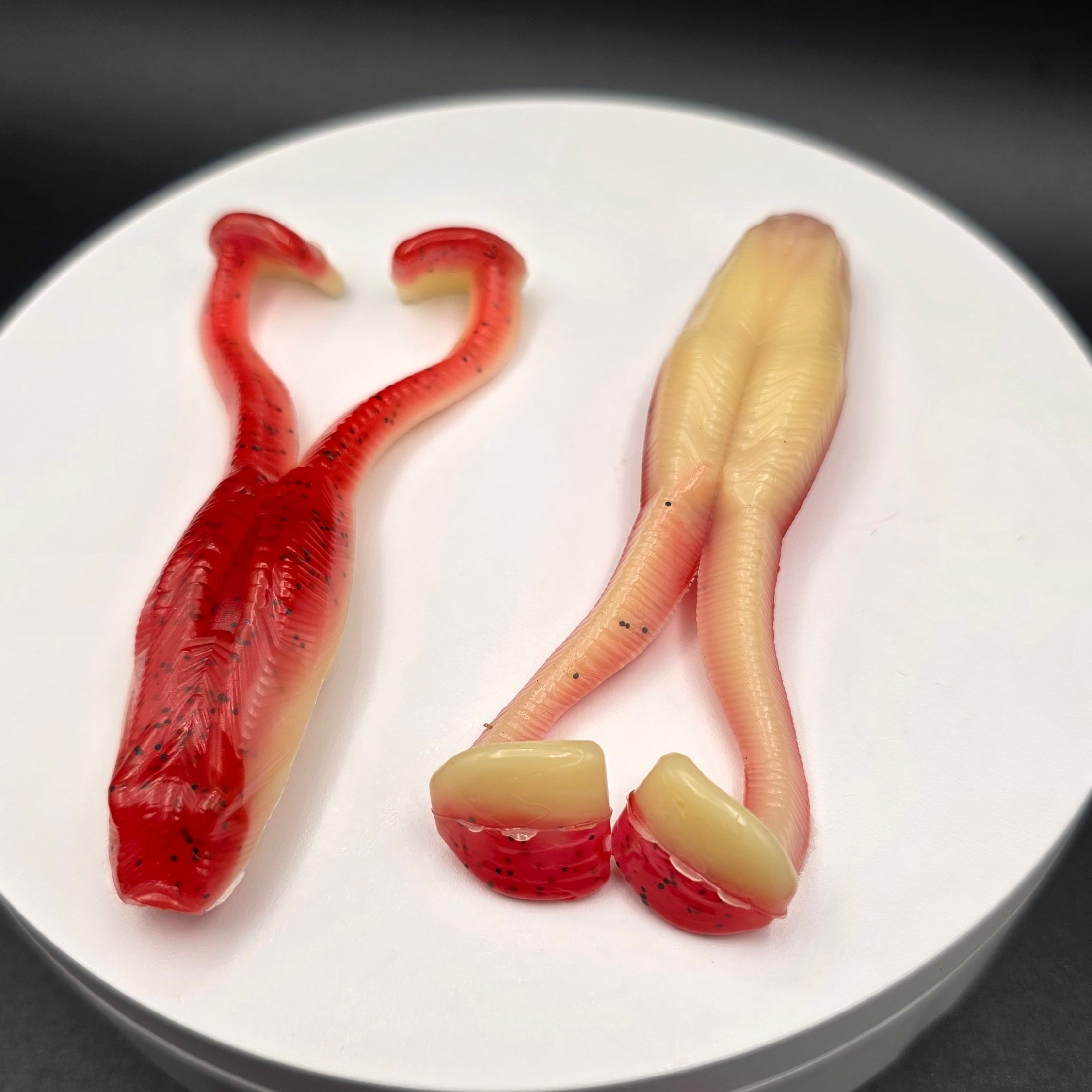 Cherry Bomb and Bone colored fishing lures with glitter on a white circular base against a dark background