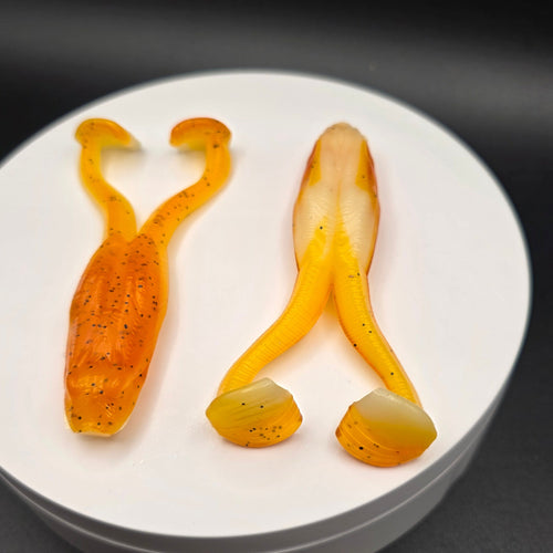 Orange and Bone colored fishing lures with blue glitter on a white circular base against a dark background