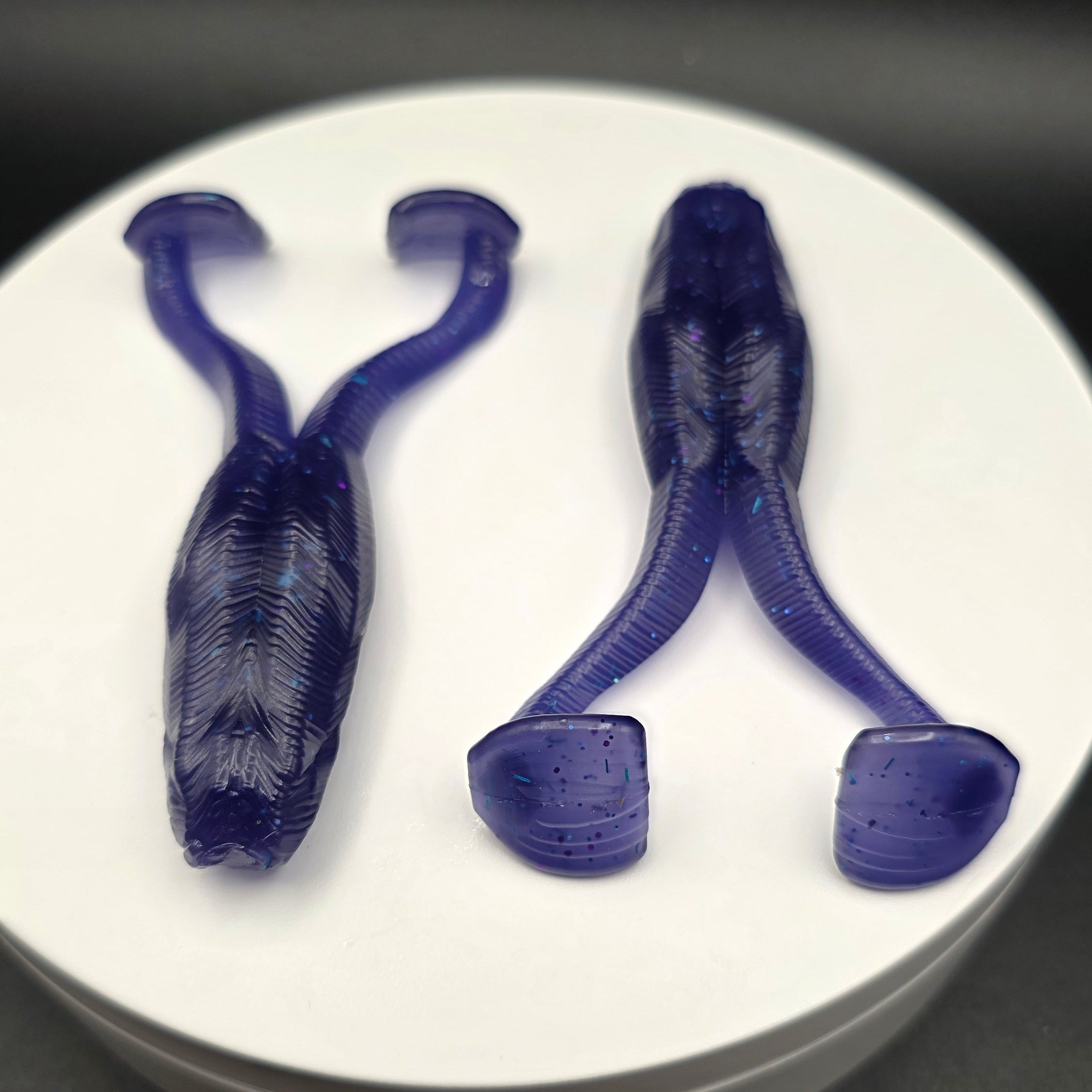 Purple June Bug fishing lures with blue glitter on a white circular base against a dark background
