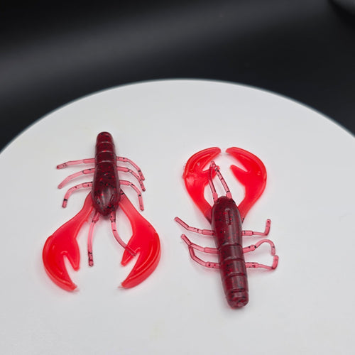 Two red crawfish lures on a white circular mat with a black background